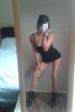 Birmingham escort poses and takes a selfie in black vest and boots