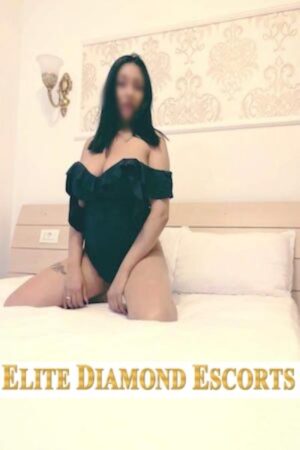busty black haired Nottingham escort kneeling on her bed