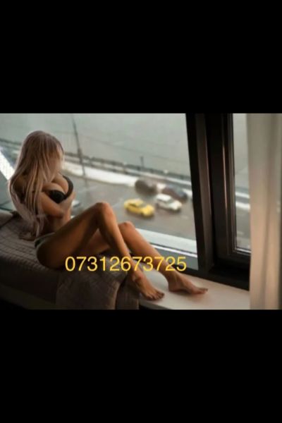 busty Reading escort posing by a high up window