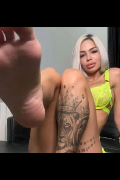 Deea Lux Noblehill Escort in bright yellow bra showing leg tattoo